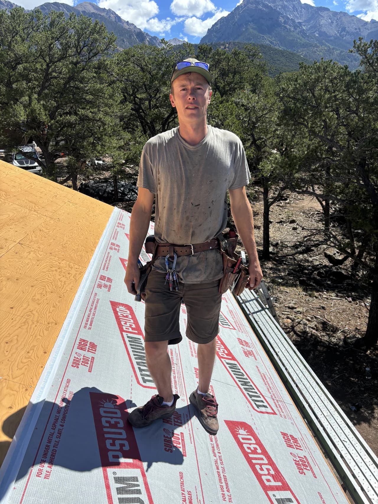 Joshua standing on a roof under construction, with mountains behind him