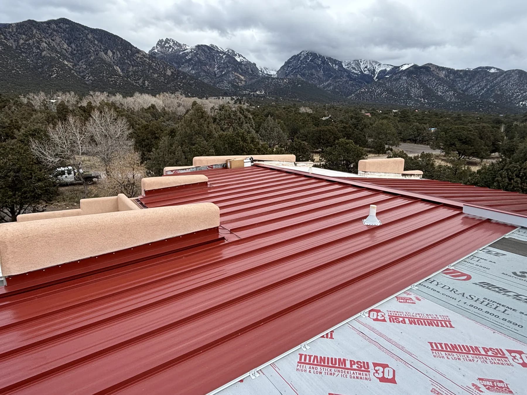 Barn-red standing-seam roof installation in progress below the mountains near Crestone