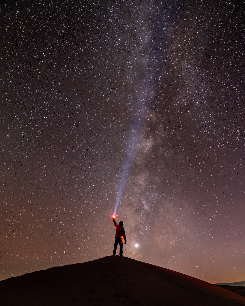 A person holding a light up to a star lit sky in the great sand dunes