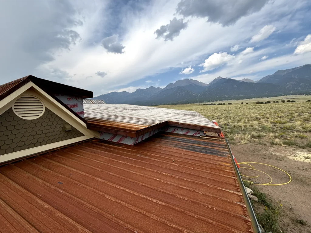 A roof with rusted aesthetic being installed and the Sangre de Cristo mountains in the backdrop