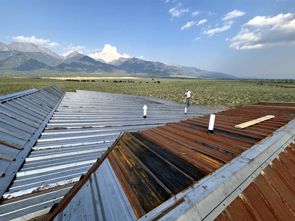 A roof with rusted aesthetic being installed and the Sangre de Cristo mountains in the backdrop