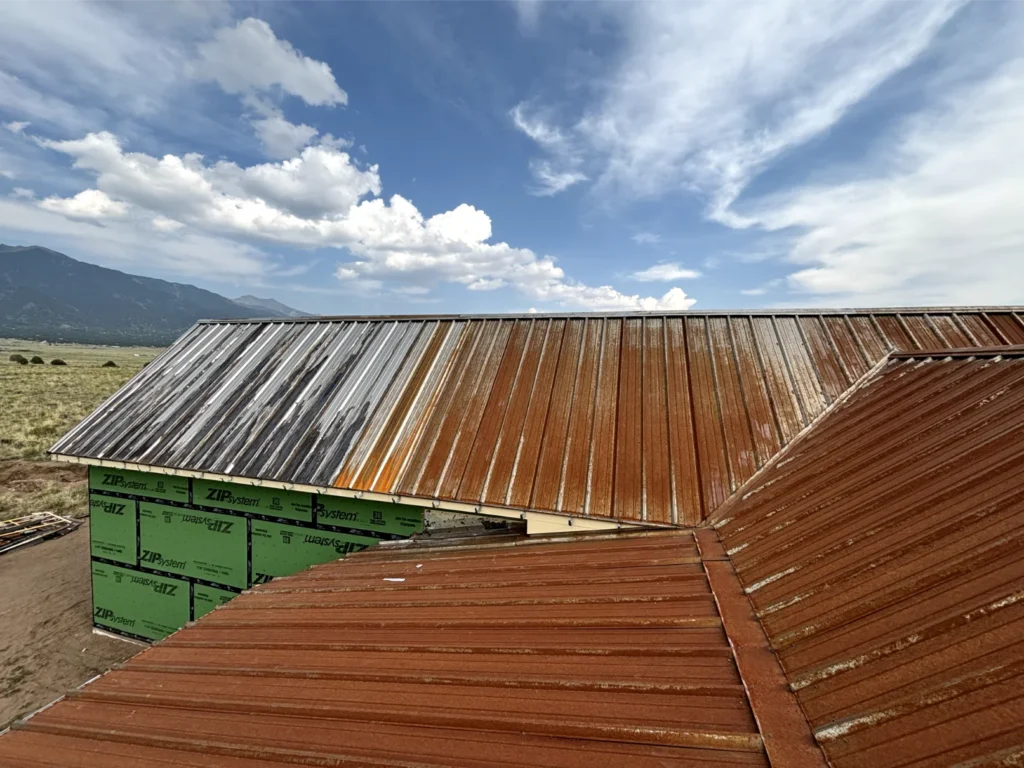 A new roof with rusted aesthetic being installed and the Sangre de Cristo mountains in the backdrop